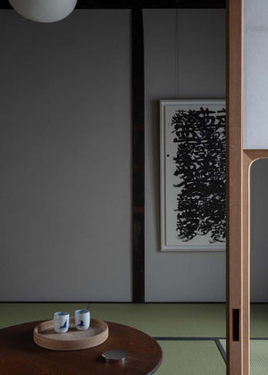 Tea set on a wooden table with a framed black and white abstract art piece in the background.