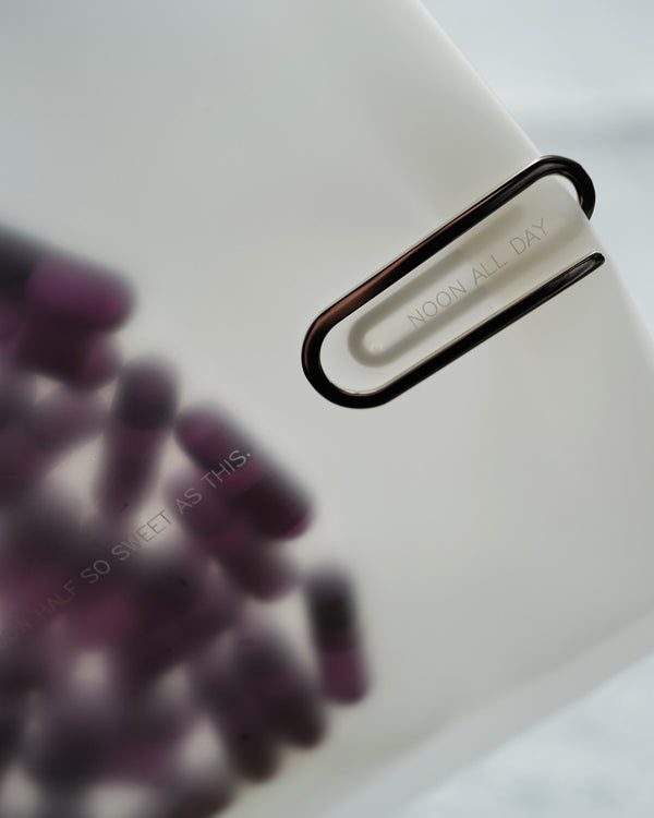 Close-up of a silver clip with 'Noon All Day' branding on a white background.