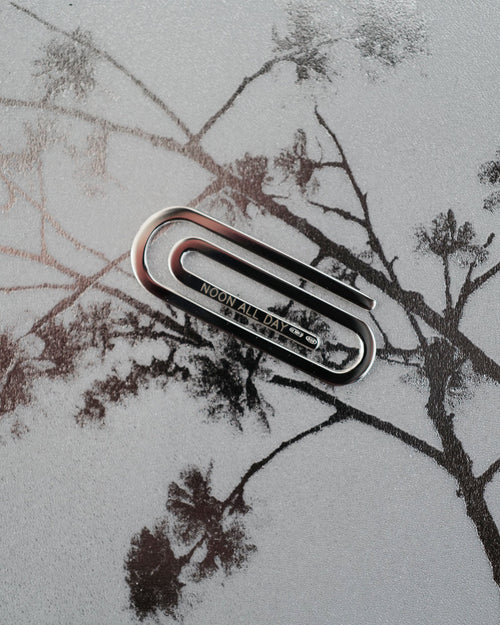 Metal paper clip on a textured surface with tree silhouettes