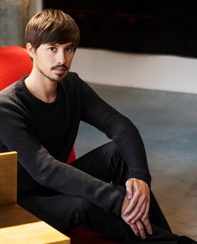 Federico Peri sitting on a red chair wearing a black sweater and pants.