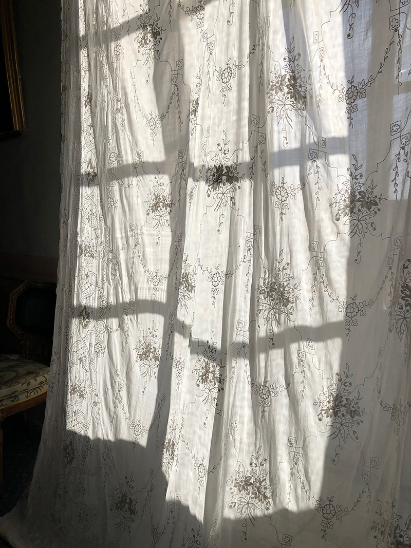 Sheer white curtain with floral pattern in a room with shadows cast on it