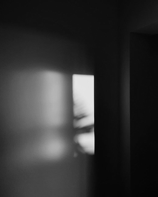 Dark room with light filtering through a window, creating shadows on the wall.