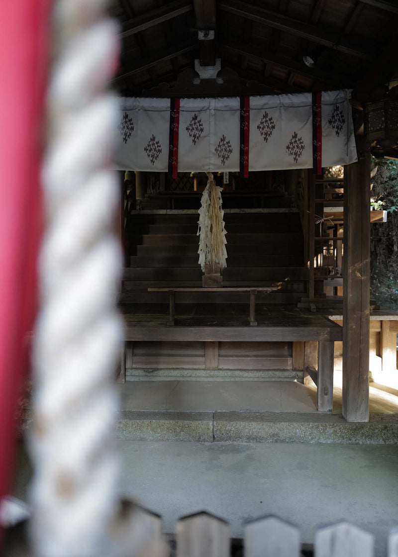 Traditional wooden shrine with white curtains and a hanging decoration, framed by a white rope.