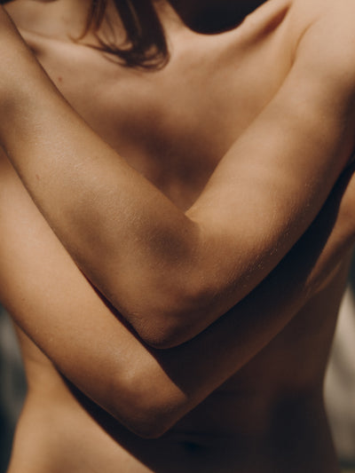 A womans torso with arms crossed in dappled sunlight