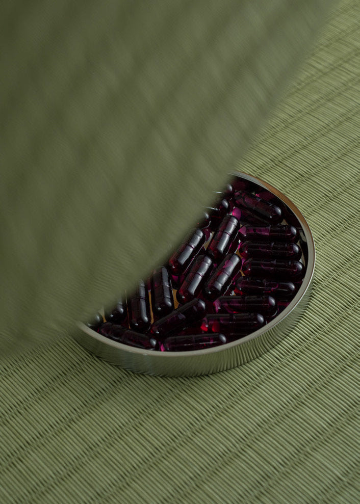 Silver food supplement container with magenta capsules on a green tatami 