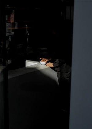 Person sitting at a table in a dimly lit room with a coffee cup on the table.