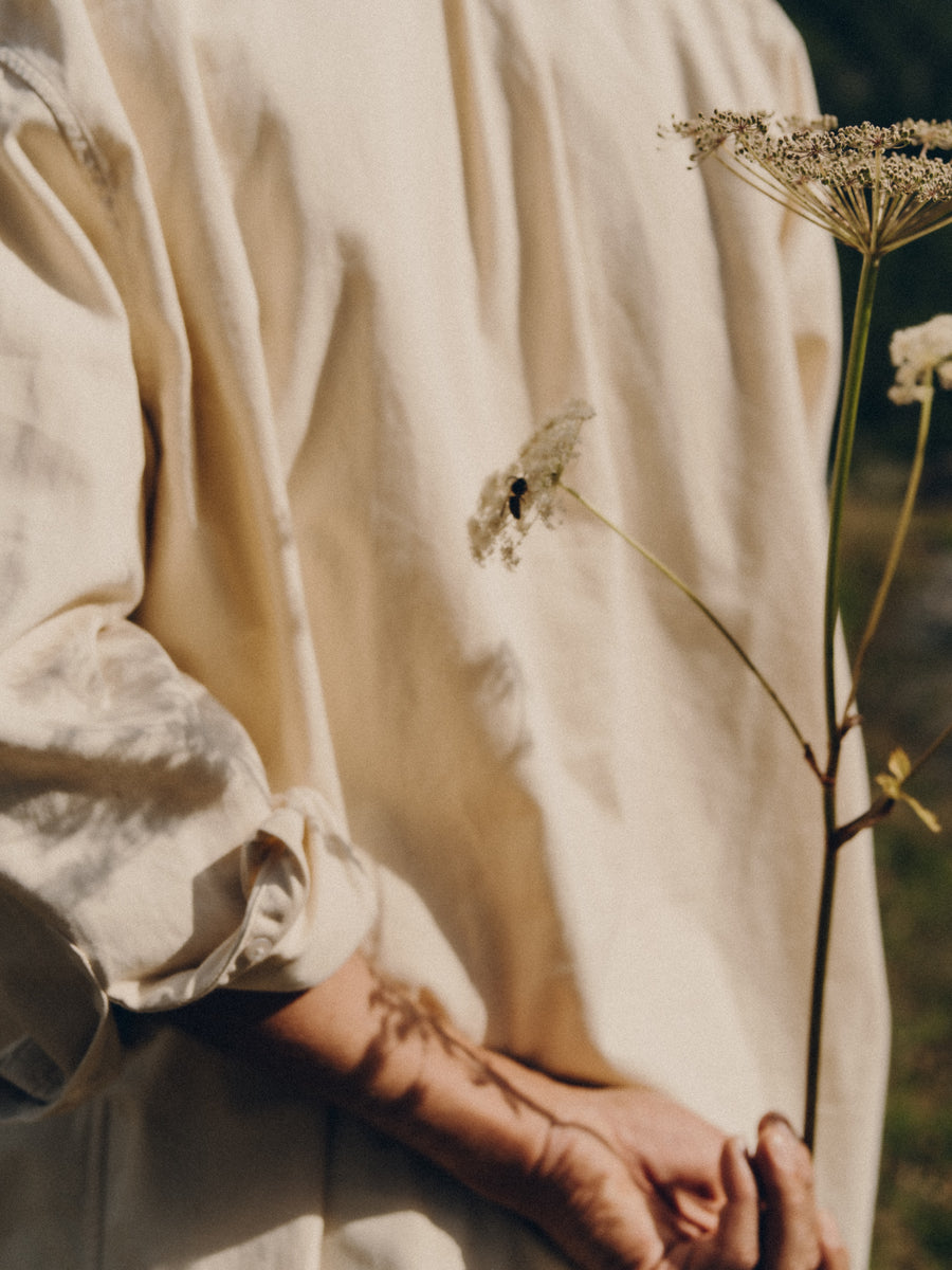 Person wearing a light-colored shirt holding a delicate flower with a blurred background