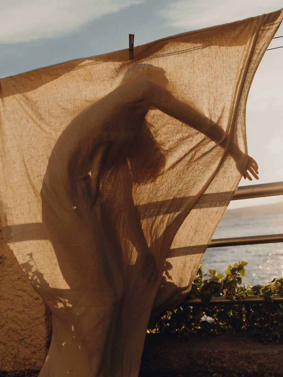 A woman stands behind a sheet on a washing line with sunlight shining through