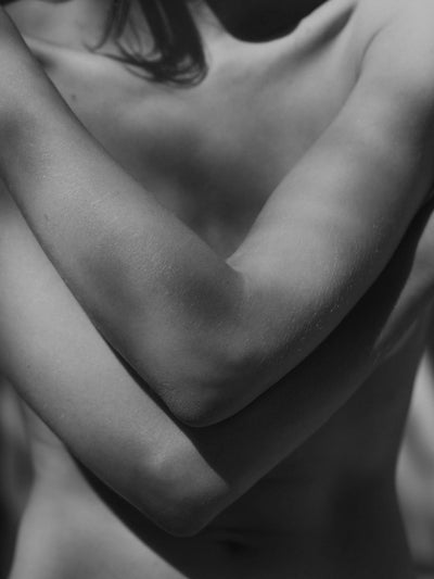 A womans torso with arms crossed in dappled sunlight
