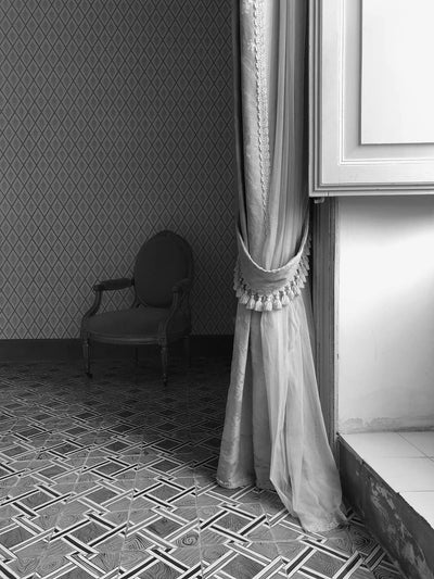 Decorative curtain with tassel tieback in a room with patterned wallpaper and tiled floor.