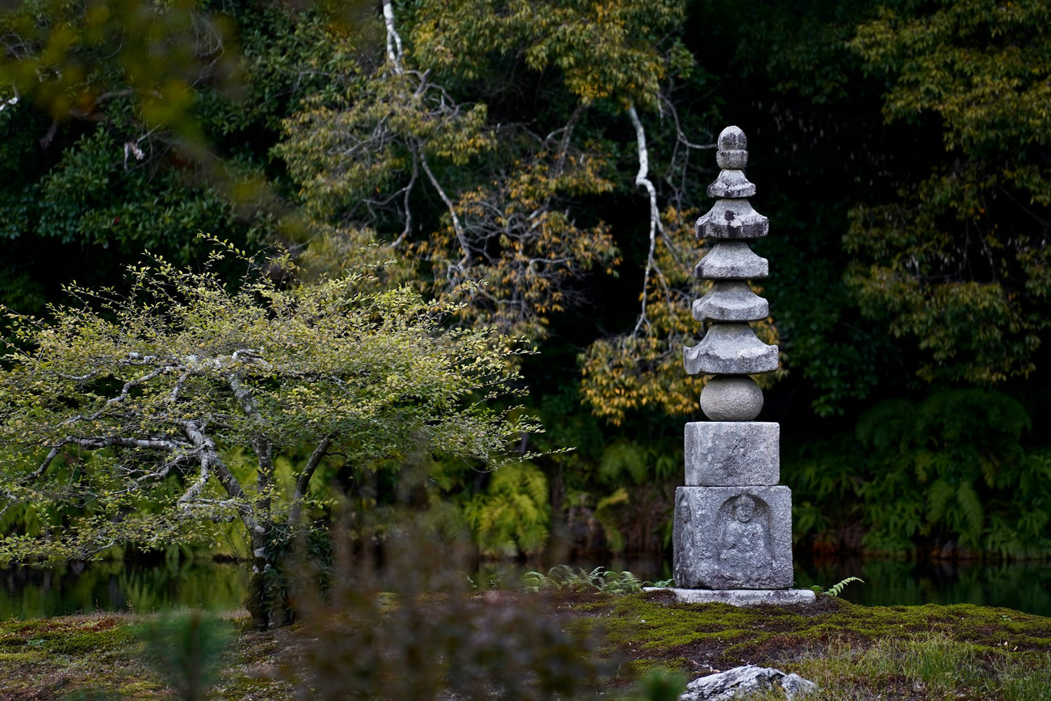 Stone pagoda in a forest setting with trees and greenery.